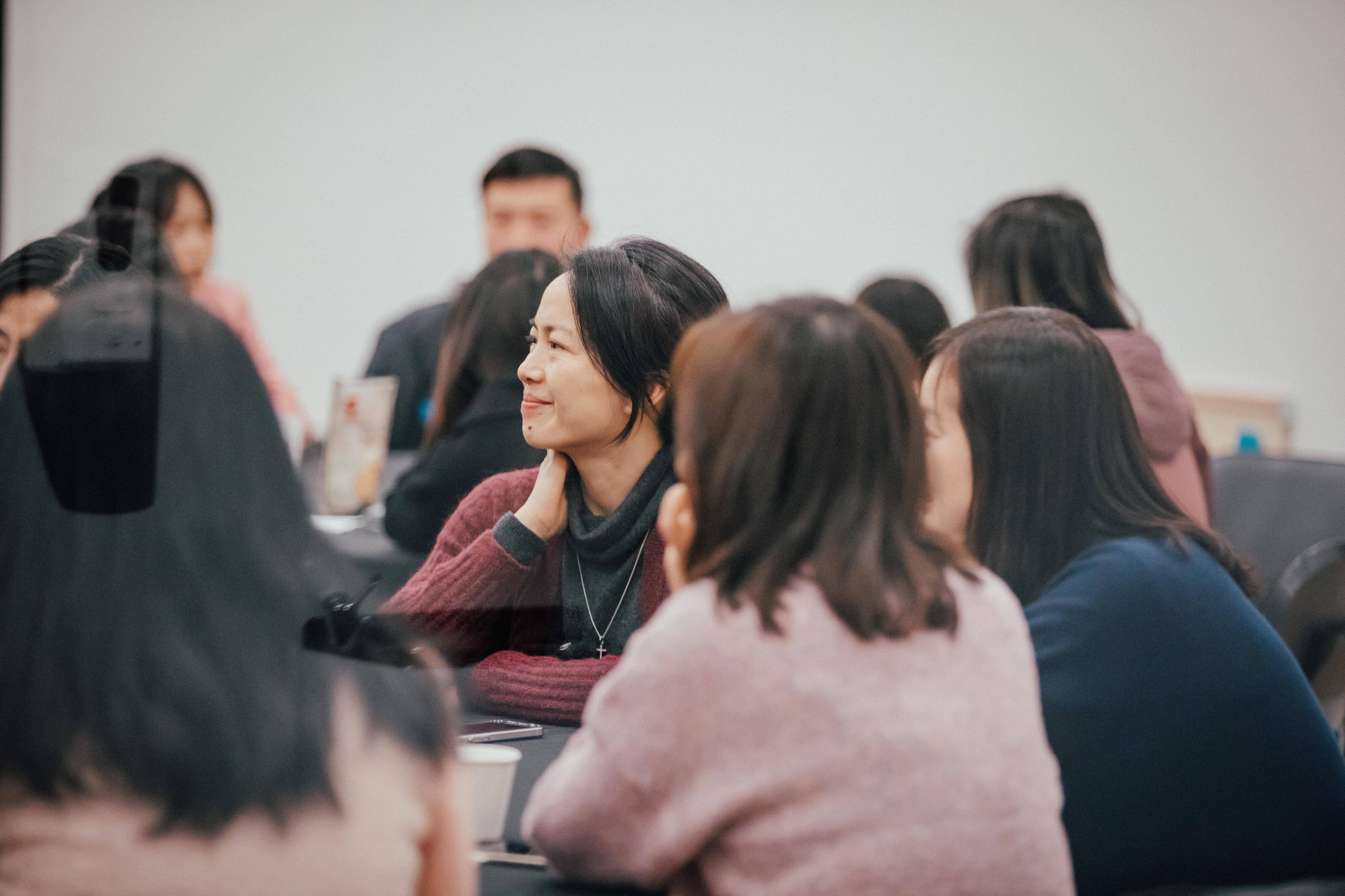 People sitting at a table during a Night School course with a woman softly smiling as she listens to the presenter